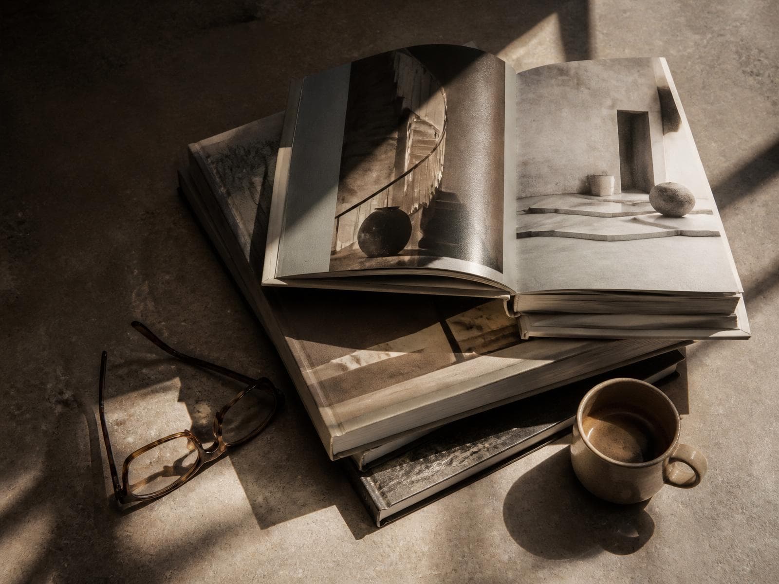 Overhead editorial still life of art and architecture books on a concrete surface, catching afternoon light.
